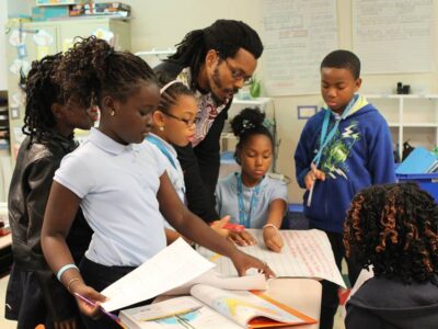 Bomani and students looking at rap they wrote on a big piece of paper in a classroom